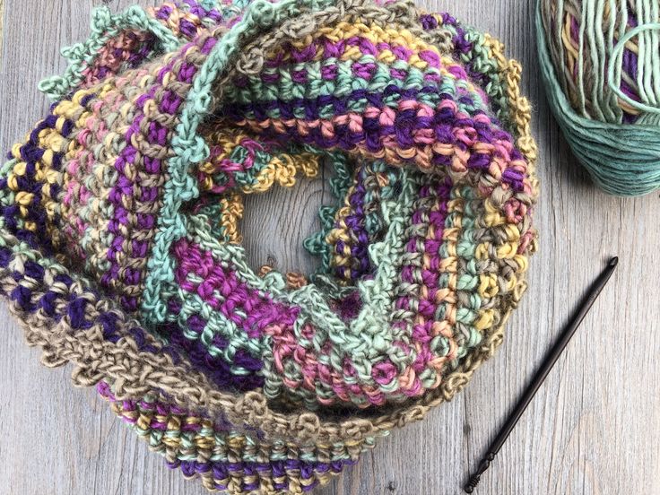 a crocheted scarf next to a ball of yarn on a wooden table with knitting needles