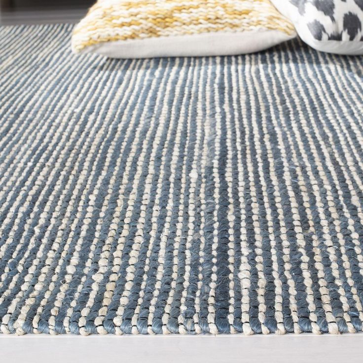 a blue rug with yellow and white pillows on it in front of a bed frame