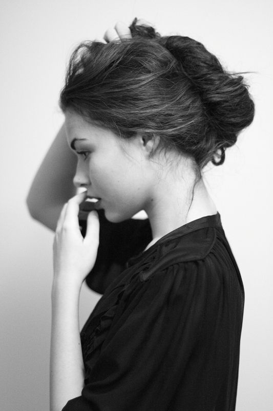 a woman is talking on her cell phone while wearing a black shirt and standing in front of a white wall