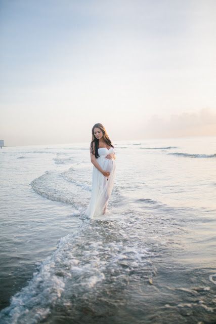 a pregnant woman standing in the water at the beach