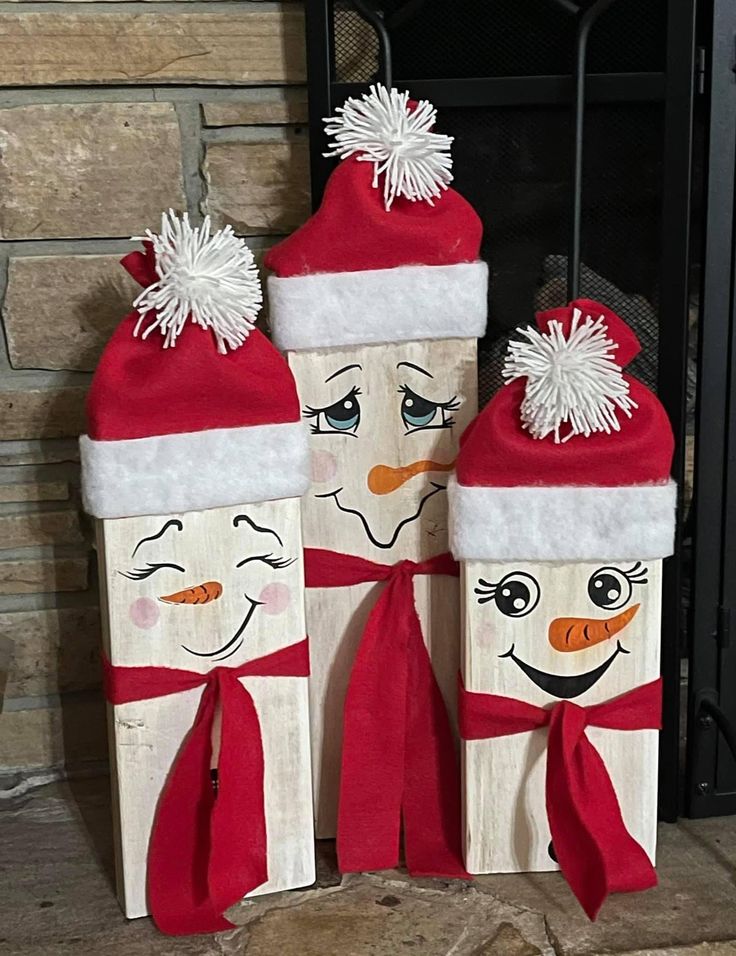 two wooden blocks decorated with snowmen wearing hats and scarfs, standing next to a fireplace