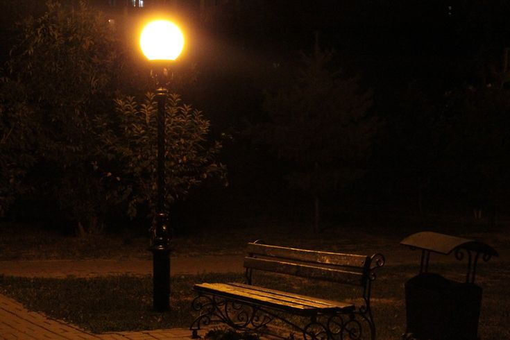 a park bench sitting on top of a wooden floor next to a street light at night