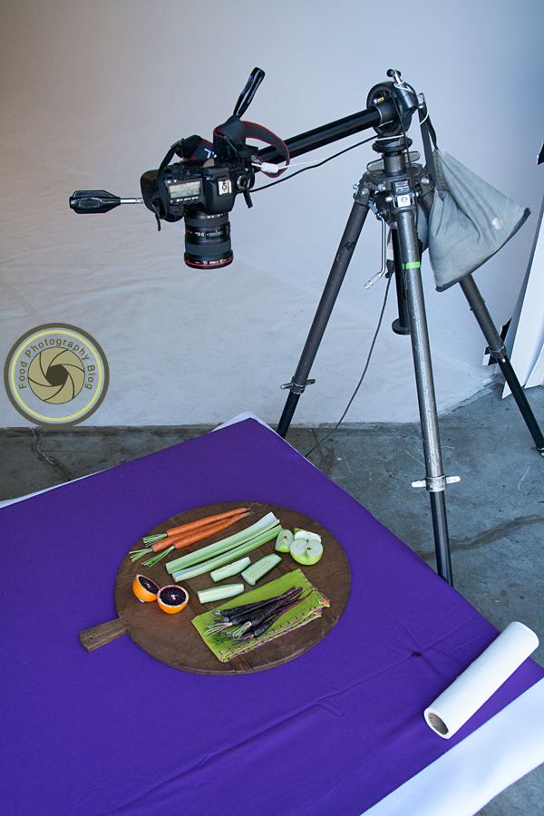 a camera is set up to take pictures of vegetables on a purple mat with a knife