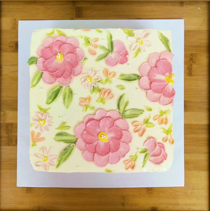 a cake decorated with pink flowers and green leaves on top of a wooden cutting board