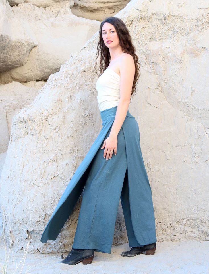 a woman standing in front of a rock formation wearing wide blue pants and a white tank top