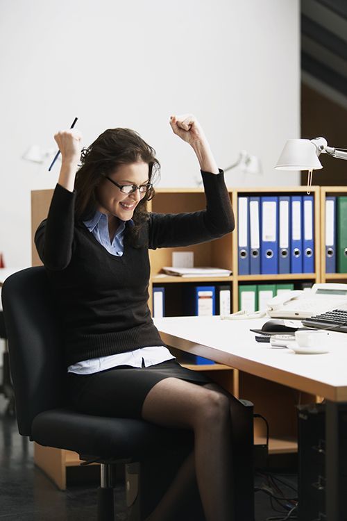 a woman sitting at a desk with her arms in the air