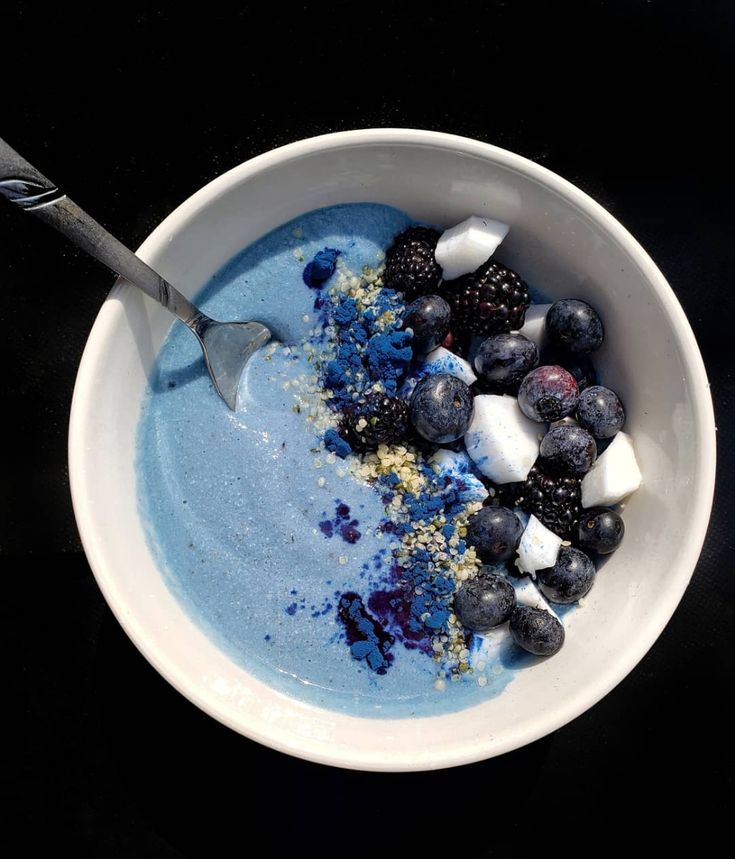 a bowl filled with blueberries and ice cream on top of a black table next to a spoon