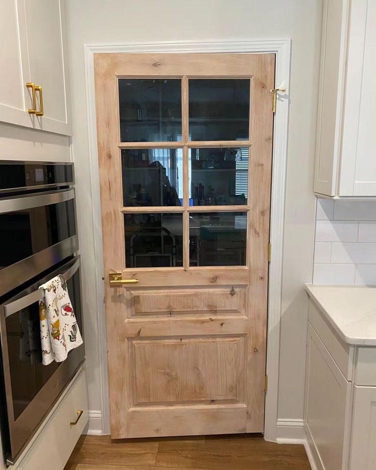 a kitchen with white cabinets and an open wooden door that leads to a stove top oven