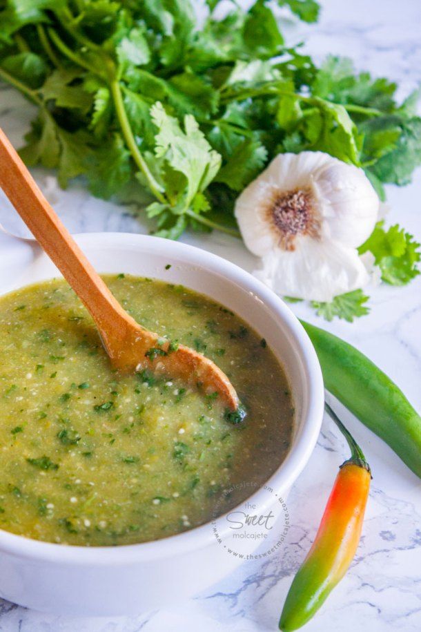 salsa verde picante in a white bowl with a wooden spoon and green peppers on the side