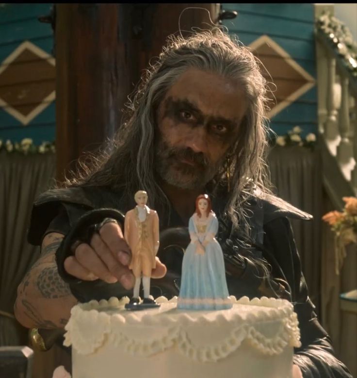 a man with long hair pointing at a cake