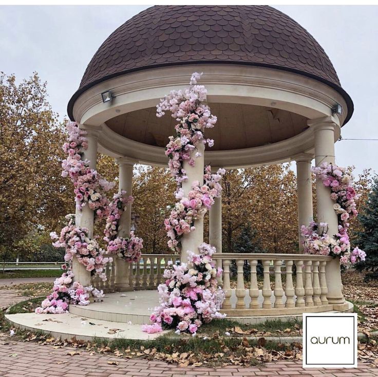 an outdoor gazebo with pink flowers on the top and bottom, surrounded by leaves