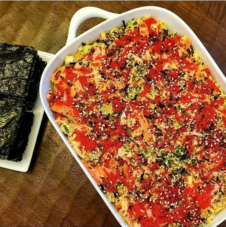 a casserole dish with meat and vegetables in it next to a plate of greens