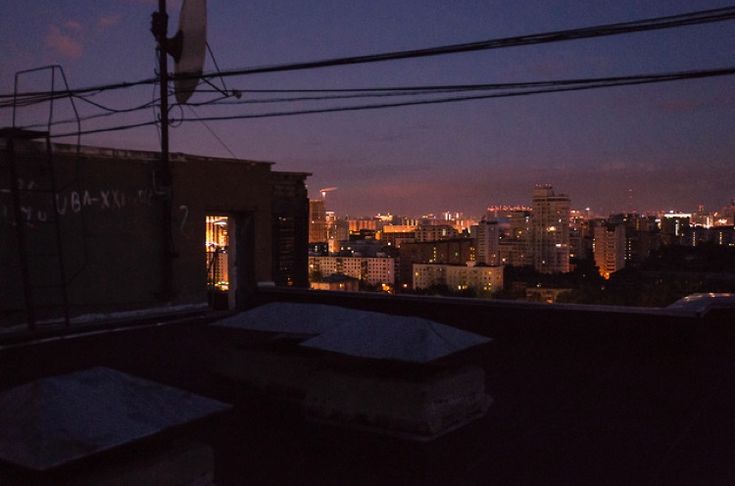 the city skyline is lit up at night with buildings in the foreground and power lines above