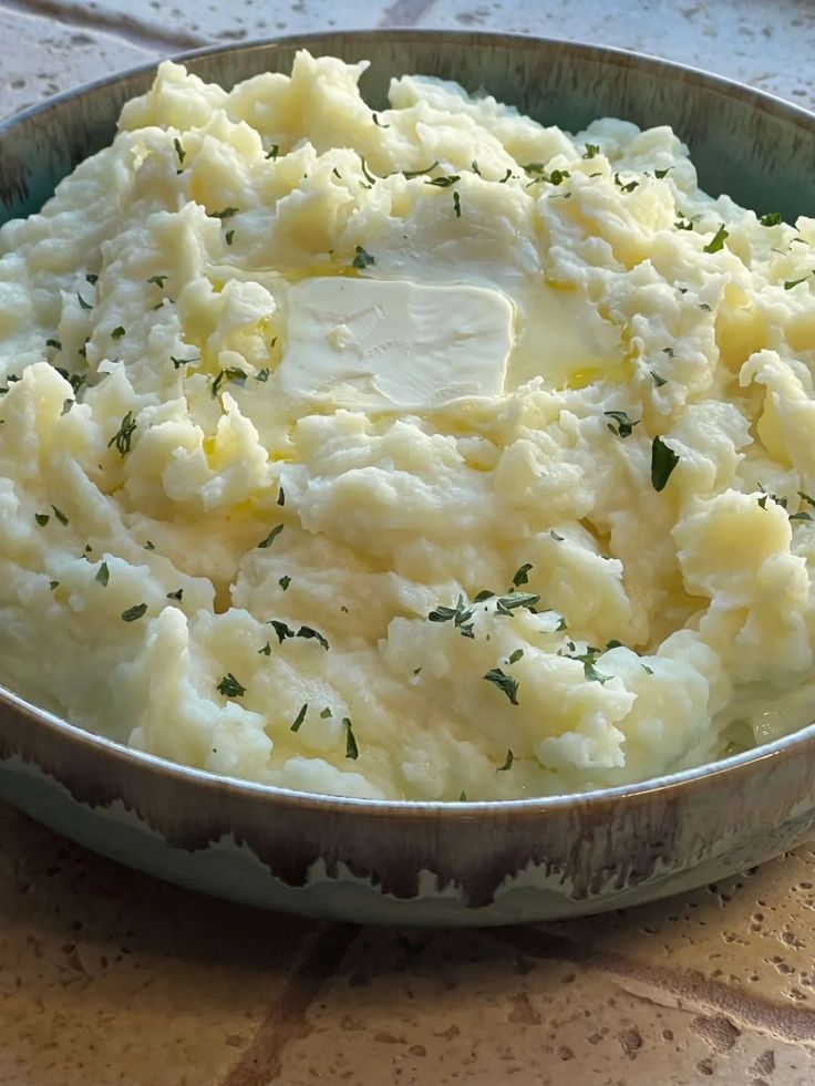 mashed potatoes with butter and parsley in a metal bowl on a tile table