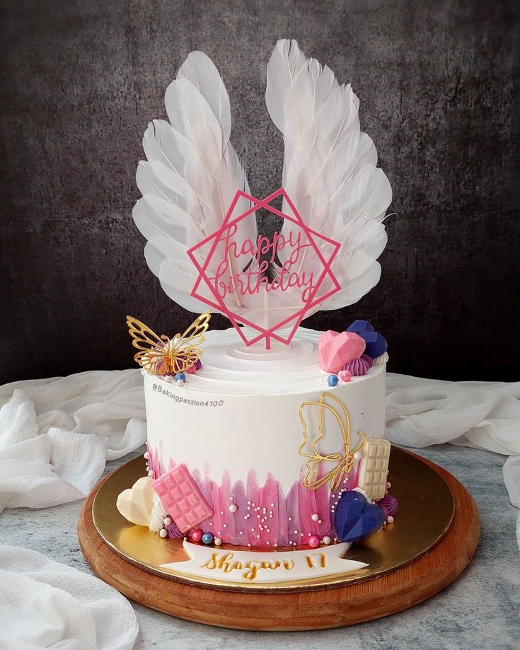 a white cake with pink frosting and angel wings on top