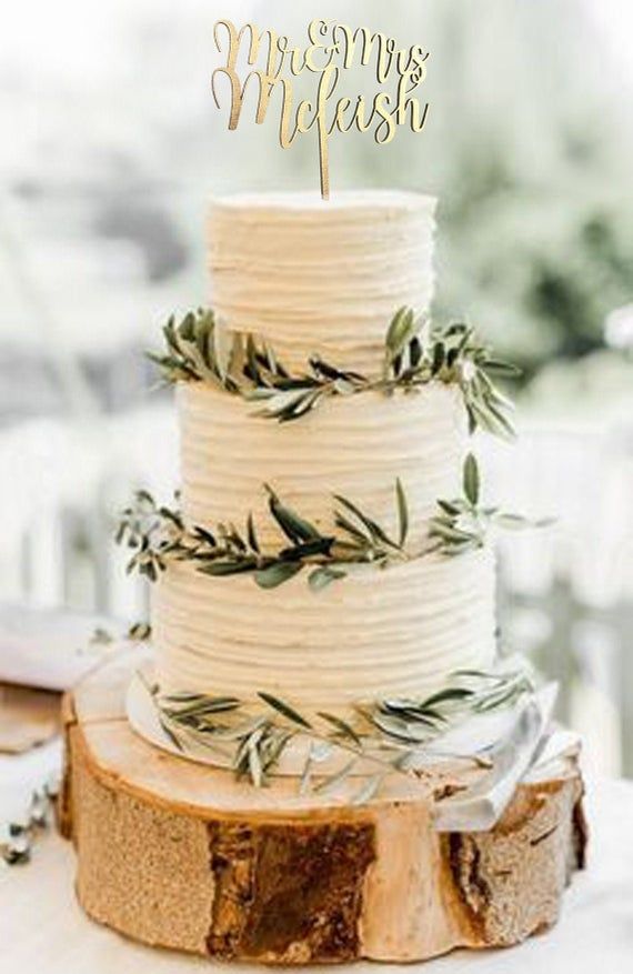 a white wedding cake with greenery on top sits on a wooden slice at the reception table