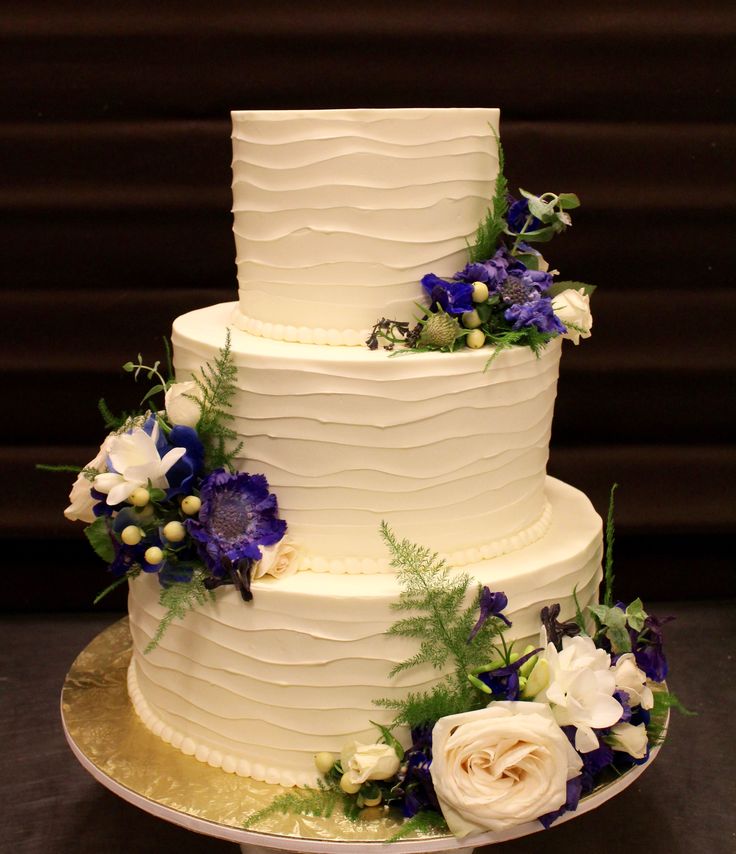 a three tiered white wedding cake with blue and white flowers