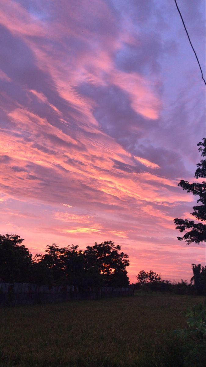 the sky is pink and purple as the sun sets in the distance behind some trees