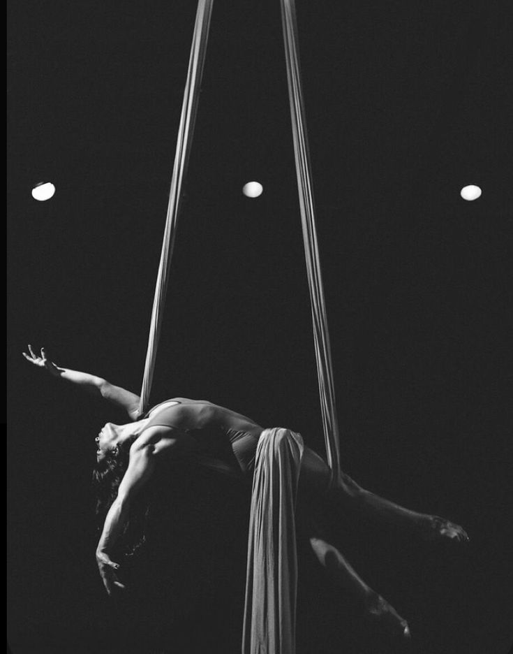 a woman is suspended upside down on a pole with two lights in the dark behind her