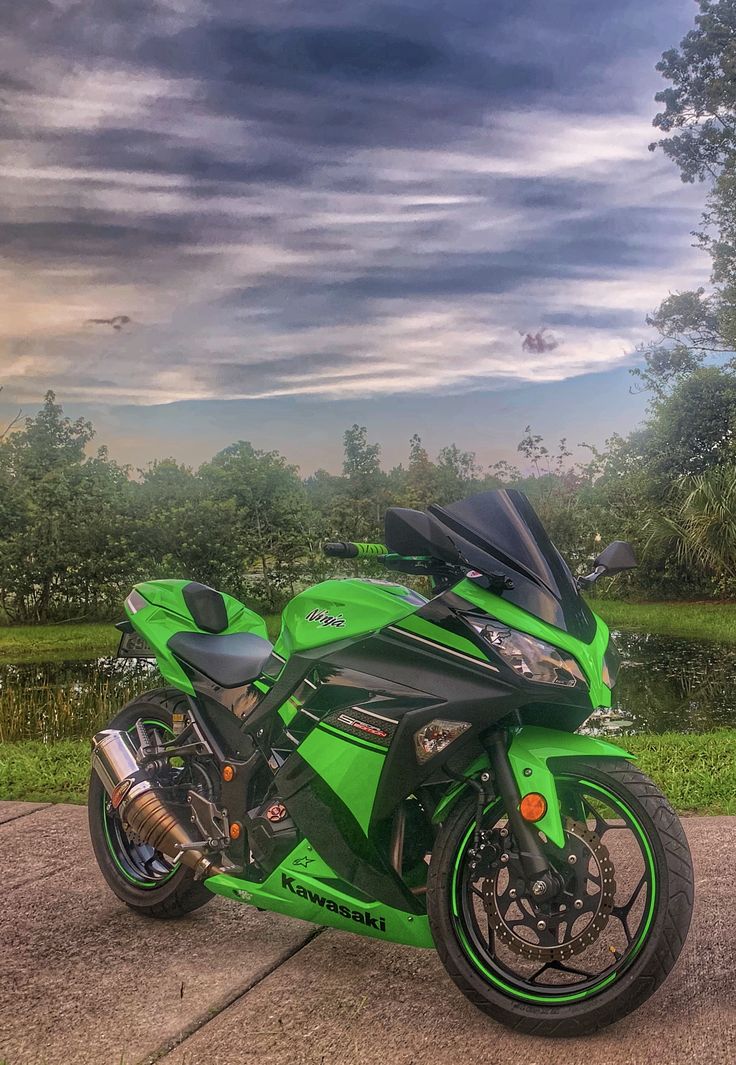 a green and black motorcycle parked on the side of a road next to a body of water