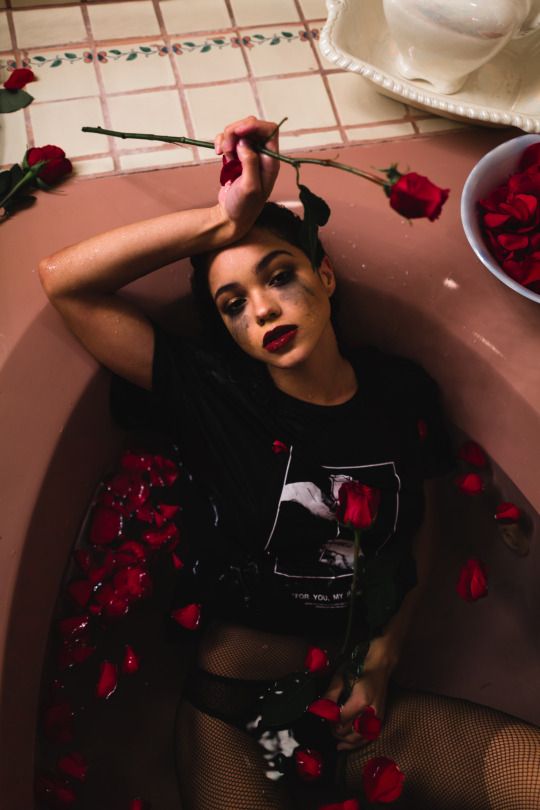 a woman laying in a bathtub with rose petals on the floor next to her