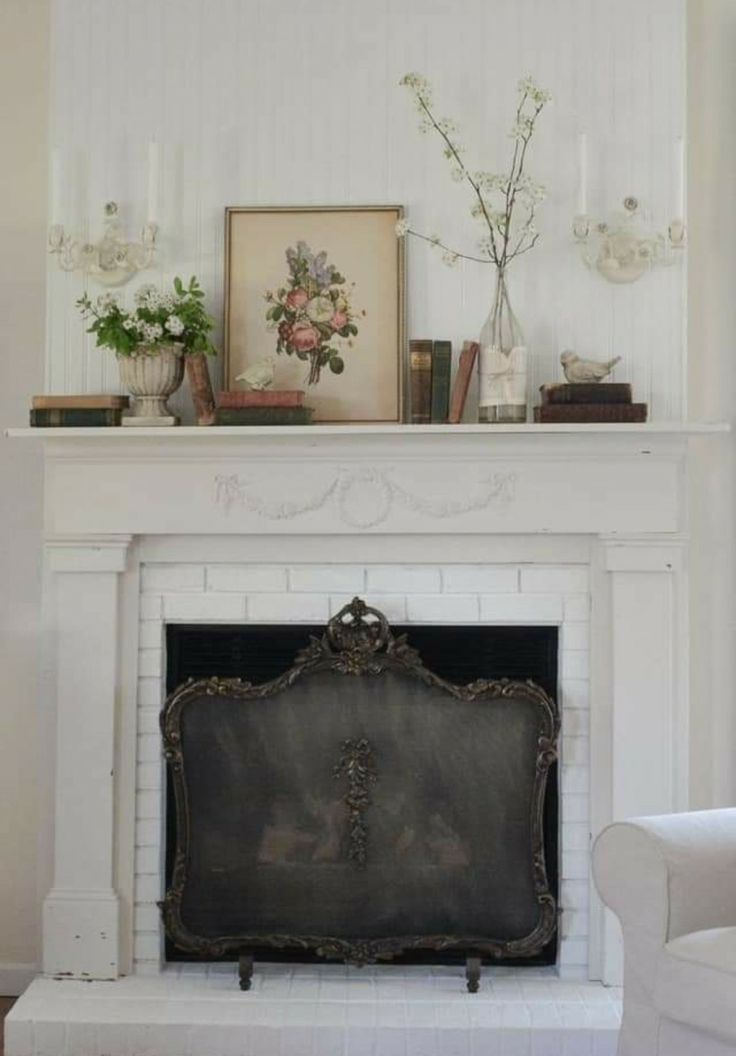 a white fireplace with flowers and pictures on the mantle