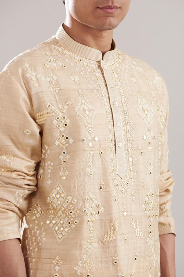 Beige tussar silk kurta with dori and mirror embroidered geometric motifs. Comes with pyjama with side pockets.
Components: 2
Pattern: Embroidered
Type Of Work: Dori, Mirror
Neckline: Mandarin collar
Sleeve Type: Full
Fabric: Tussar silk
Color: Beige
Other Details: 
Product Weight : 0.7 Gms
Closure : 
Kurta : Front buttons
Pyjama : Front button and zip
Occasion: Mehendi and Puja - Aza Fashions Tussar Silk Kurta, Silk Kurta, Geometric Motifs, Pyjama Set, Embroidered Silk, Mandarin Collar, Aza Fashion, Sleeve Type, Pajama Set