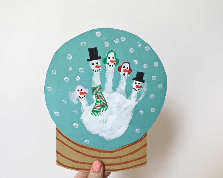 someone is holding up a paper snow globe with their handprinted snowmen in it