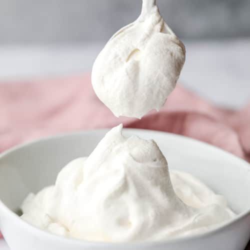 a spoonful of whipped cream in a white bowl on top of a pink towel