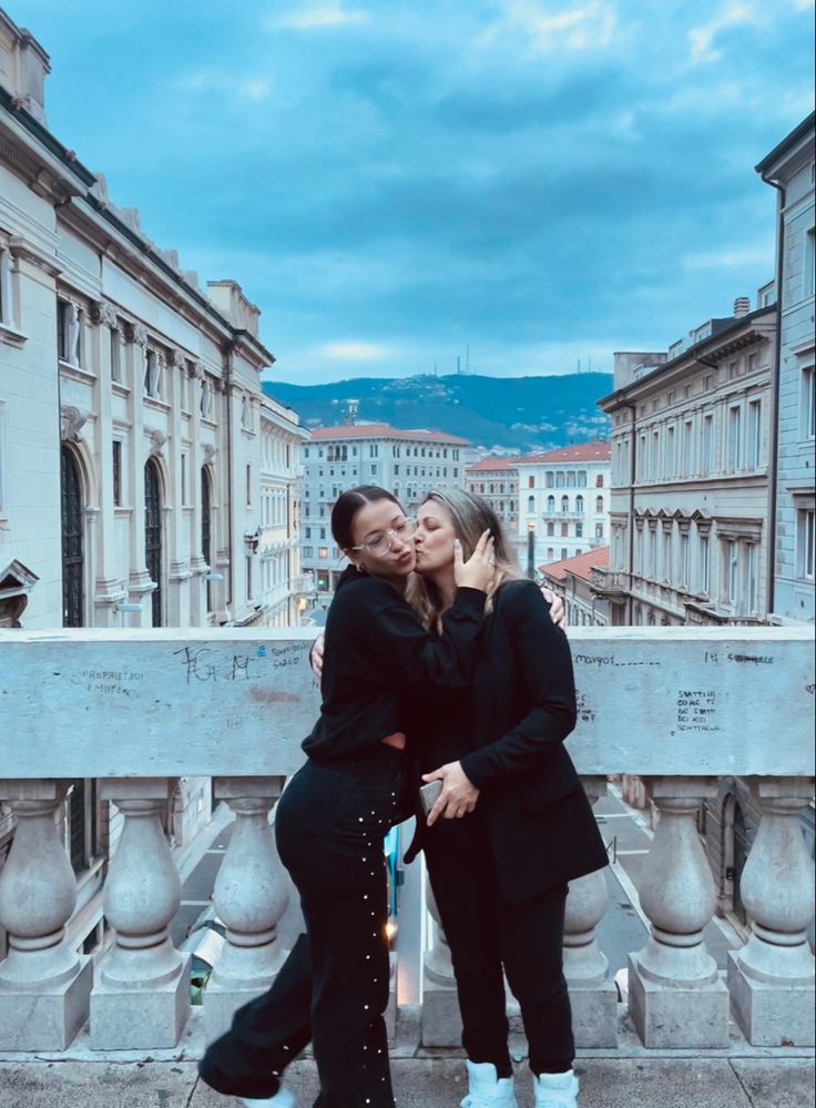 two women hugging each other in front of some buildings