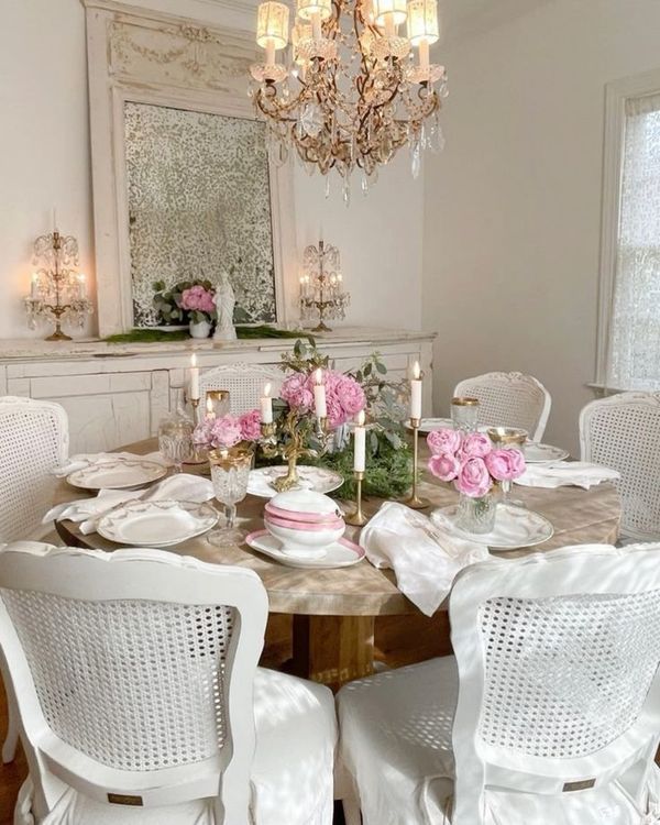 a dining room table with white chairs and pink flowers on the centerpiece, surrounded by chandeliers