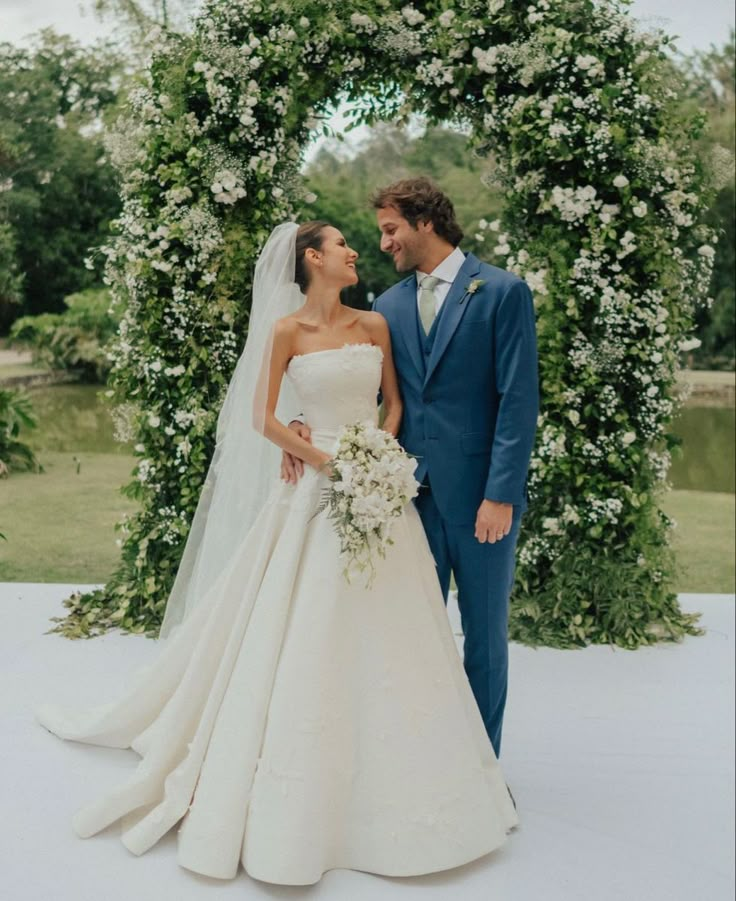 a bride and groom standing in front of an archway with white flowers on the side