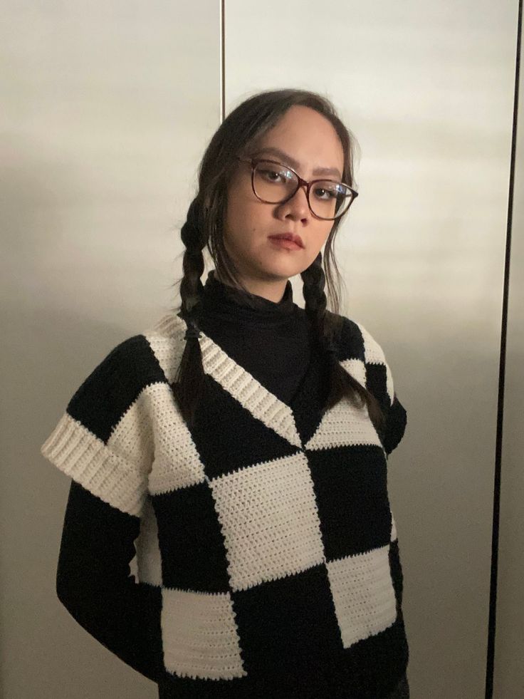 a woman wearing glasses and a black and white sweater standing in front of a wall