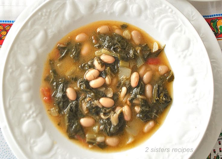 a white plate topped with beans and greens next to a bowl of soup on top of a table