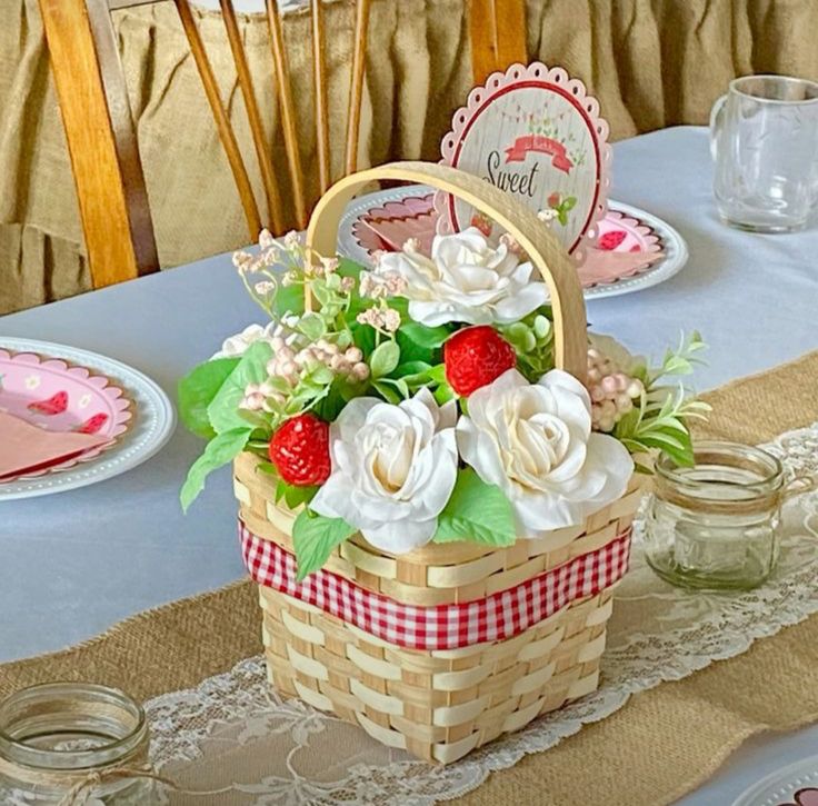 a basket with strawberries and flowers on a table set for a picnic or brunch