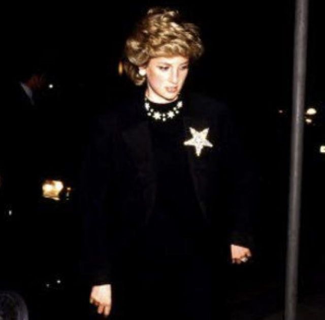 the woman is walking down the street wearing a black suit and white star brooch