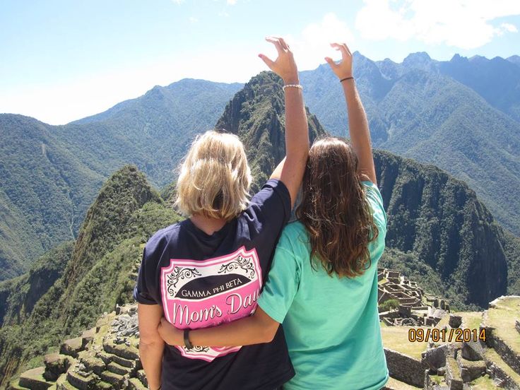 two girls standing on top of a mountain with their arms in the air