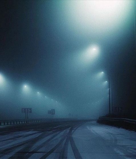 an empty road with street lights in the fog on a cold day at night time