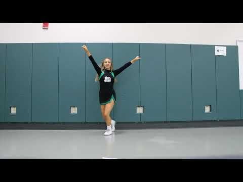 a woman in a black shirt and green skirt is dancing with her arms outstretched while wearing white sneakers