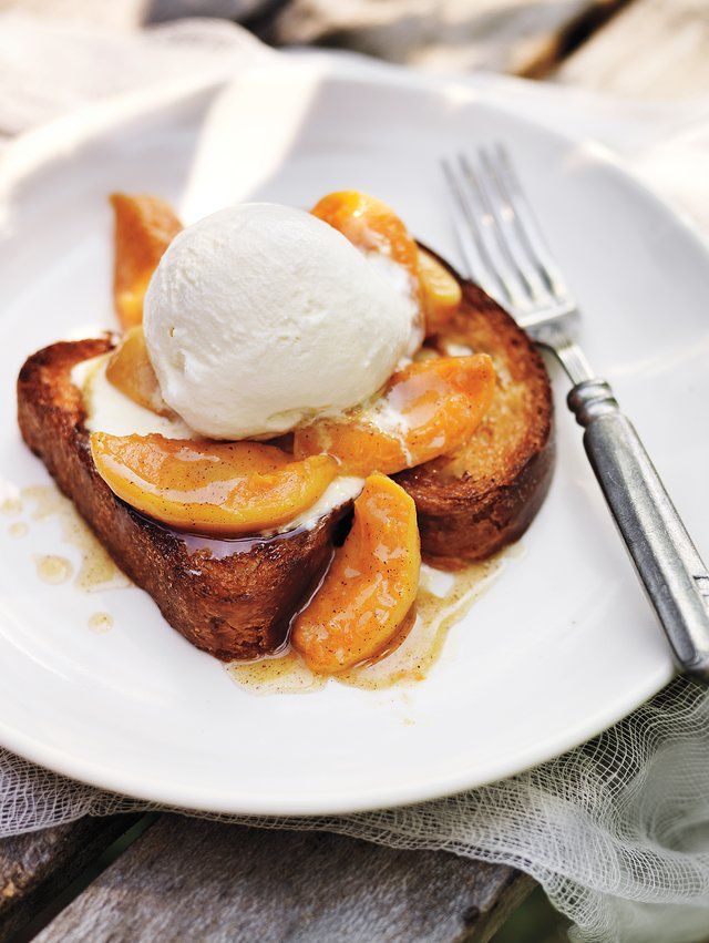 a white plate topped with french toast covered in ice cream and sliced peaches next to a fork