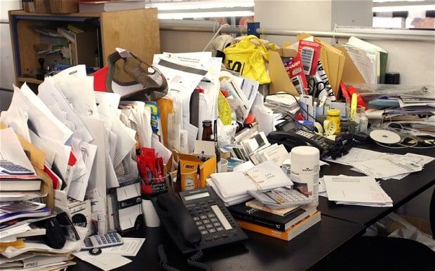 a cluttered desk in an office filled with papers and other items, including a telephone