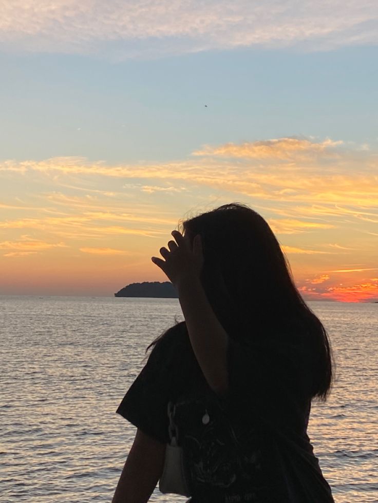 a woman standing on top of a beach next to the ocean at sunset with her hands up in the air