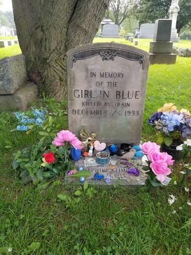 a grave in the grass with flowers around it and a tree behind it that reads, in memory of the girl'n blue