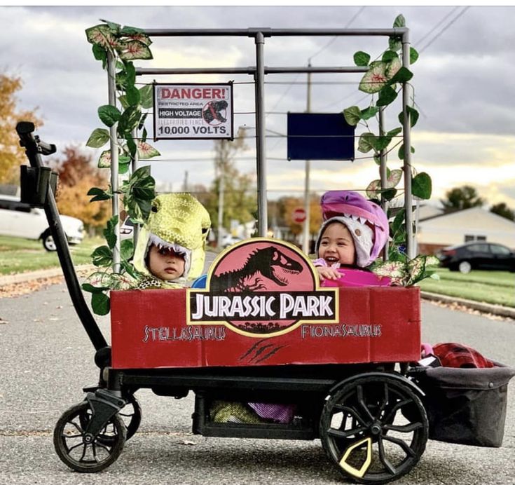 two children are riding in a dinosaur park wagon