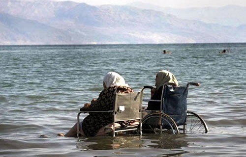 two people sitting in a wheel chair in the water