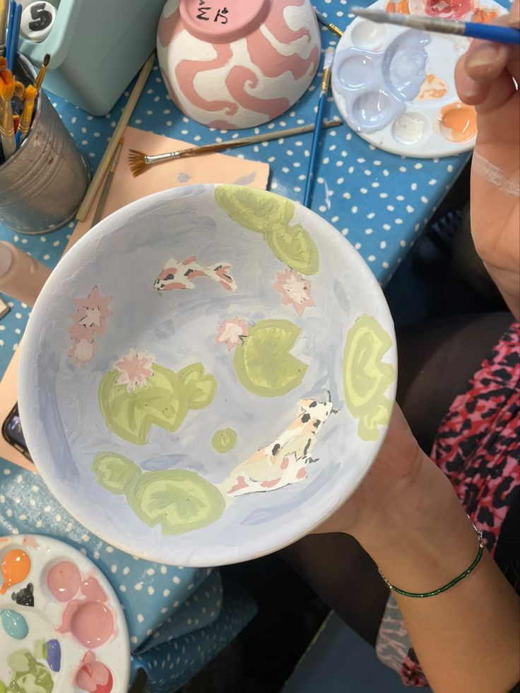 a woman is holding a bowl with water lilies painted on it while sitting at a table