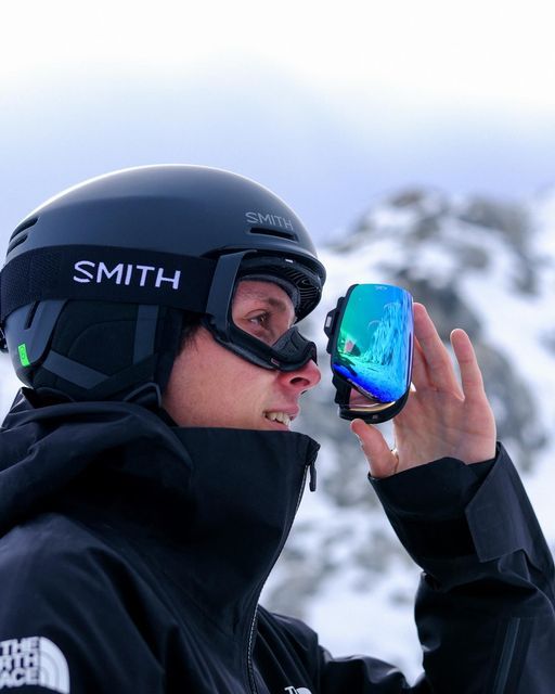 a man wearing a helmet and goggles holds up his sunglasses