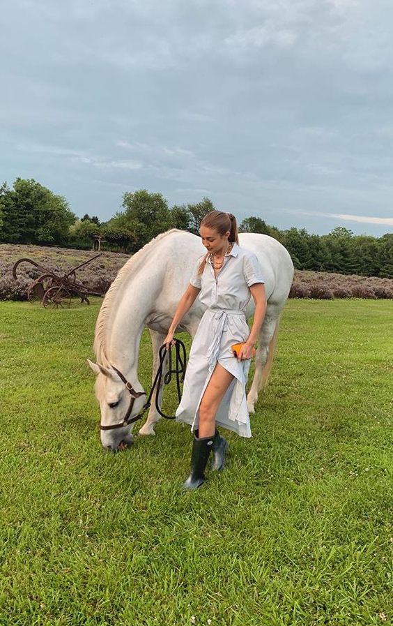 a woman standing next to a white horse on top of a lush green field