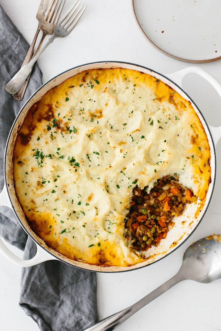 a casserole dish with cheese and meat in it on a white plate next to silverware