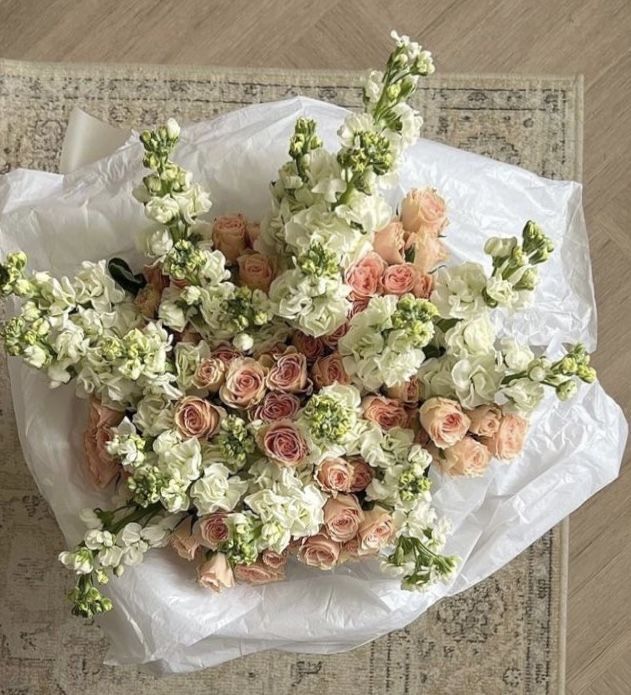 a bouquet of flowers sitting on top of a white paper bag next to a rug